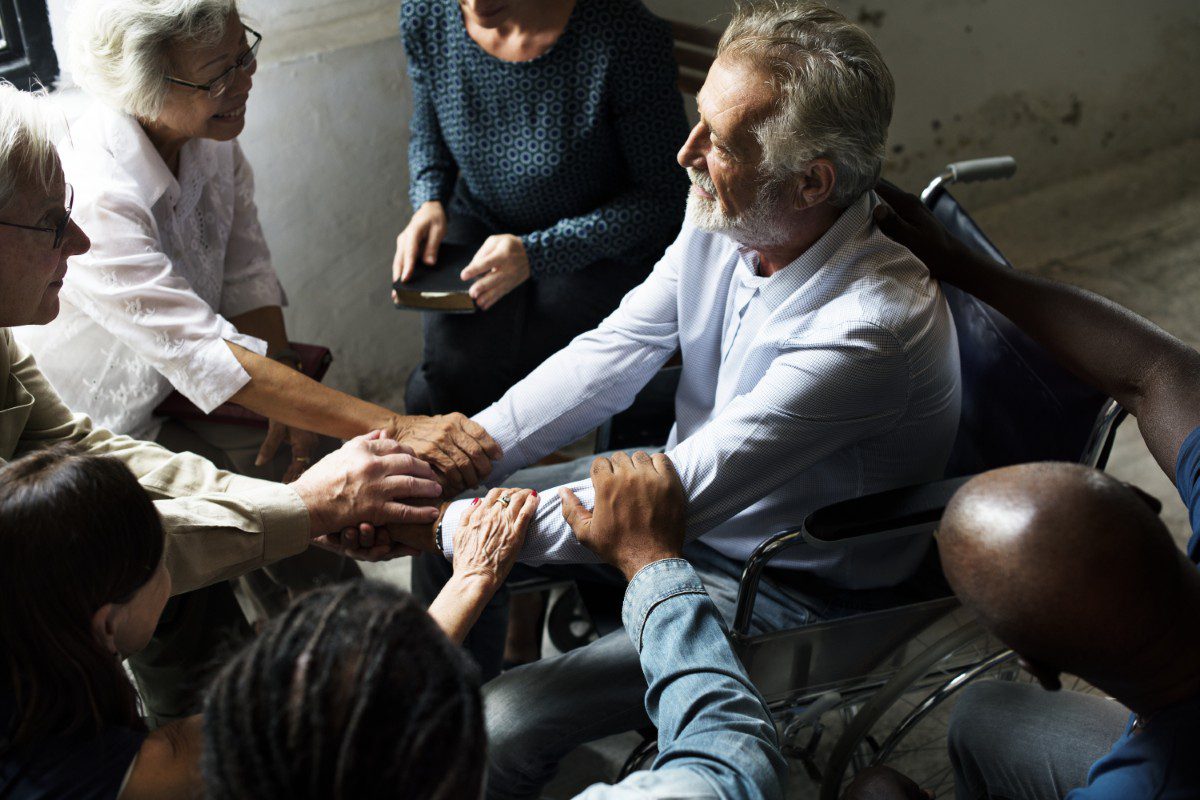 Group supporting man in wheelchair, holding hands.